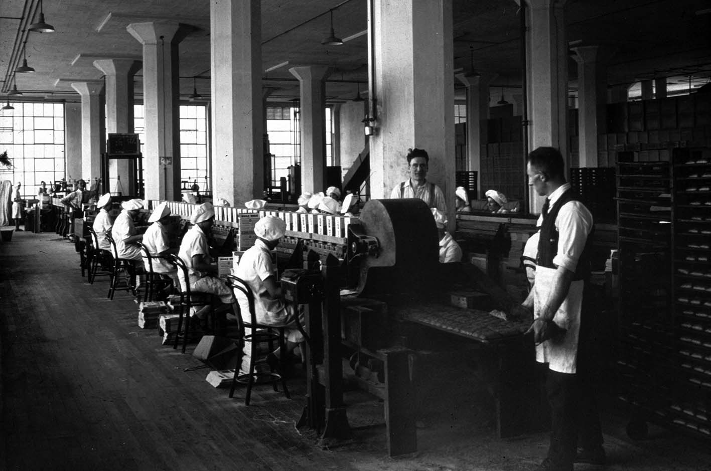 Shredded Wheat factory interior - photograph dated 1926 showing the packing line with a panner (on right) feeding a pan of 'biscuits' onto the conveyor.